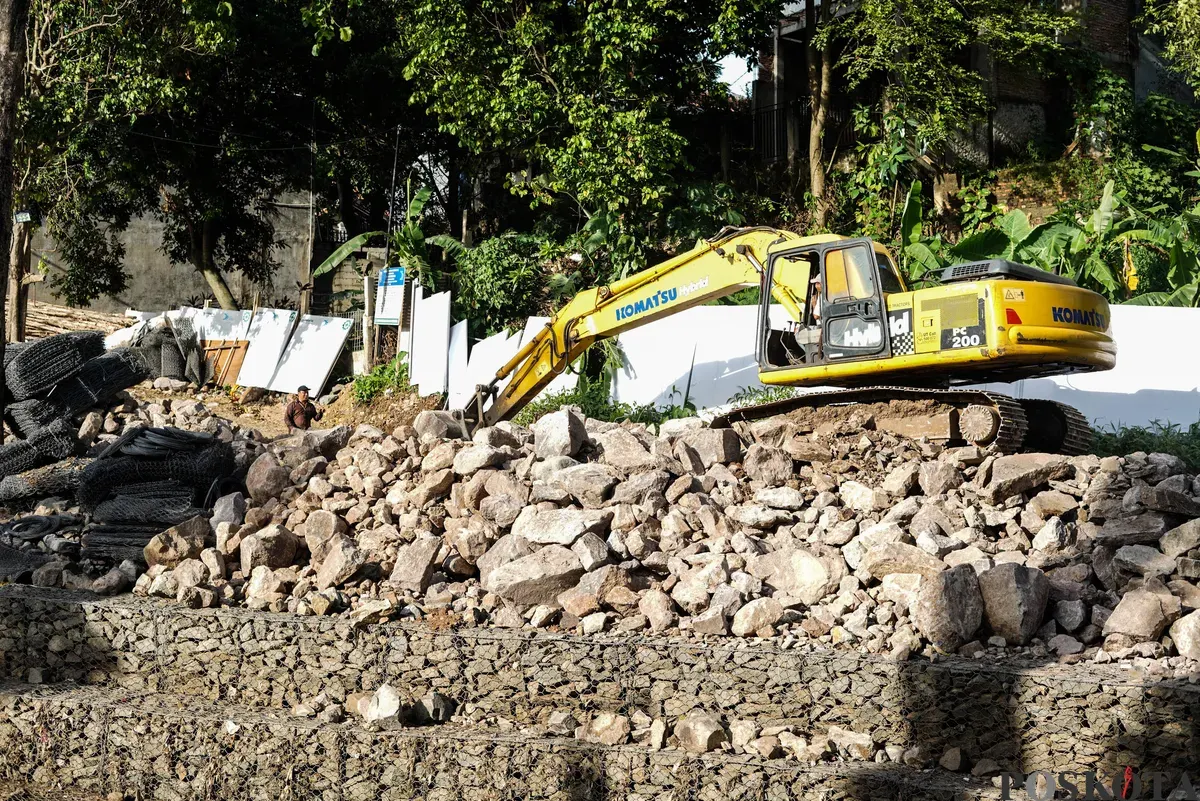 Operator eskavator memindahkan batu kali untuk proyek pembangunan turap bronjong di bantaran Kali Ciliwung, Cililitan, Jakarta, Selasa, 25 November 2025. (Sumber: Poskota/Bilal Nugraha Ginanjar)