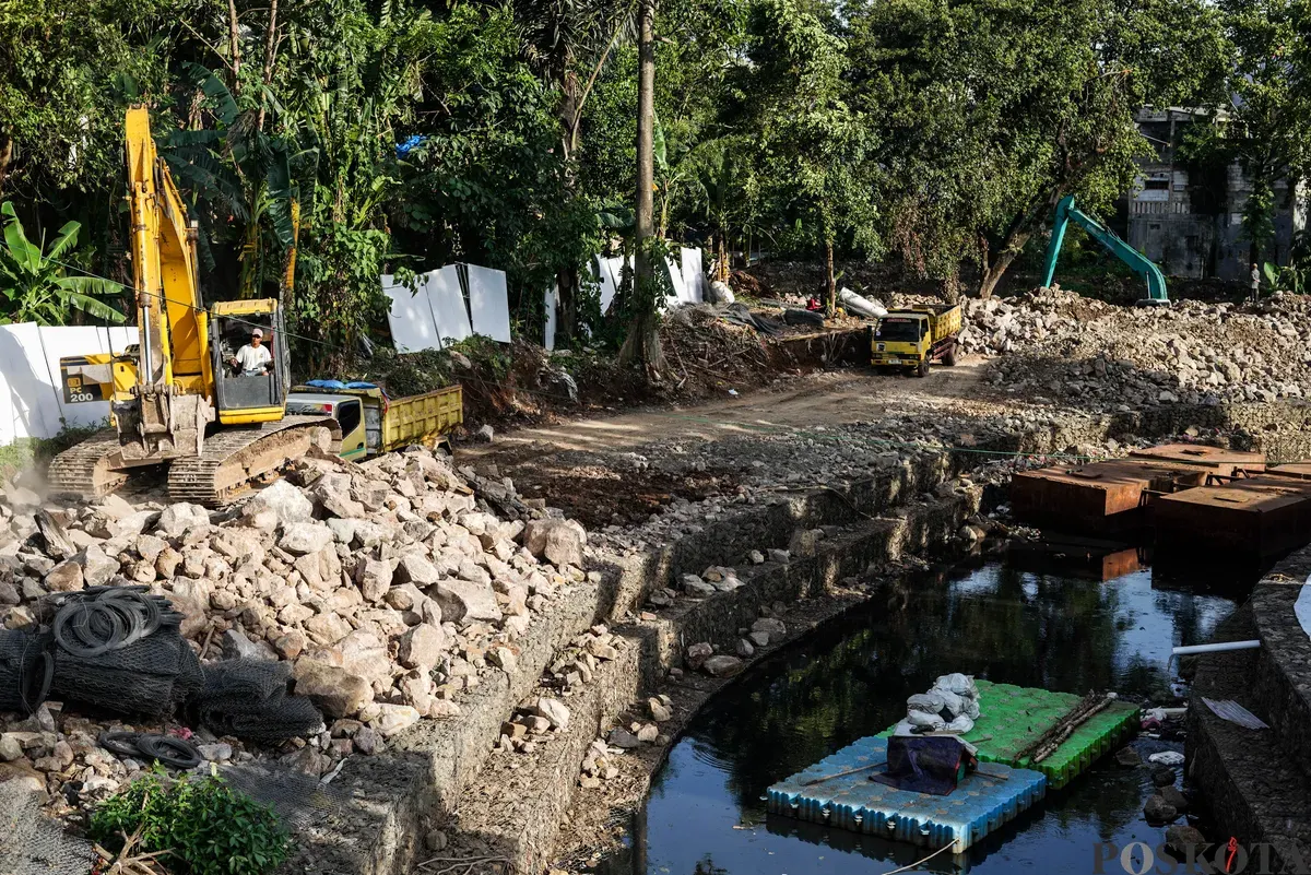 Operator eskavator memindahkan batu kali untuk proyek pembangunan turap bronjong di bantaran Kali Ciliwung, Cililitan, Jakarta, Selasa, 25 November 2025. (Sumber: Poskota/Bilal Nugraha Ginanjar)