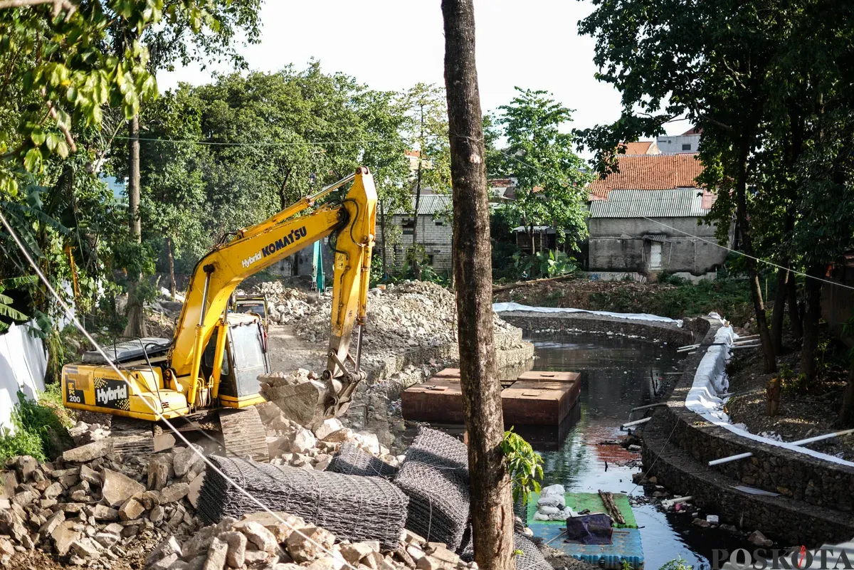 Operator eskavator memindahkan batu kali untuk proyek pembangunan turap bronjong di bantaran Kali Ciliwung, Cililitan, Jakarta, Selasa, 25 November 2025. (Sumber: Poskota/Bilal Nugraha Ginanjar)