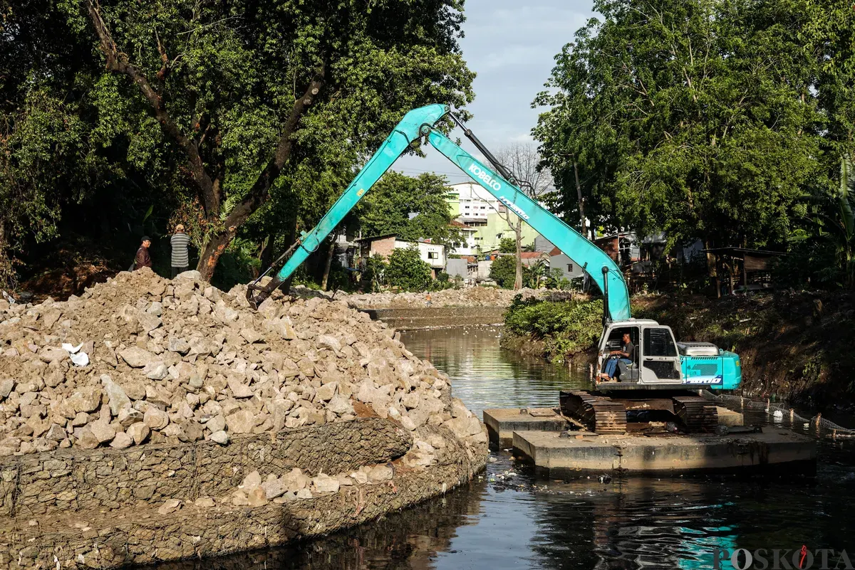 Operator eskavator memindahkan batu kali untuk proyek pembangunan turap bronjong di bantaran Kali Ciliwung, Cililitan, Jakarta, Selasa, 25 November 2025. (Sumber: Poskota/Bilal Nugraha Ginanjar)