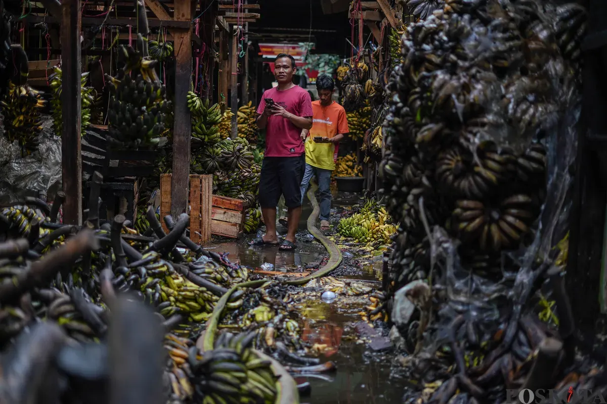 Pedagang merapihkan sisa buah-buahan yang hangus usai kebakaran di Pasar Induk Kramat Jati, Jakarta Timur, Senin, 15 Desember 2025. (Sumber: Poskota/Bilal Nugraha Ginanjar)