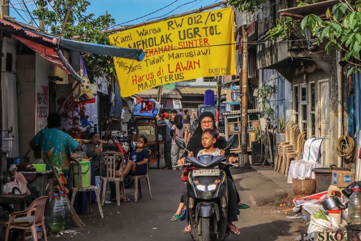 Warga beraktifitas melintasi spanduk penolakan uang ganti rugi tol Semanan Sunter di kawasan RW 09/12, Duri Pulo, Gambir, Jakarta Pusat, Selasa, 23 Desember 2025. (Sumber: Poskota/Dhiya Ahmad Fauzan)