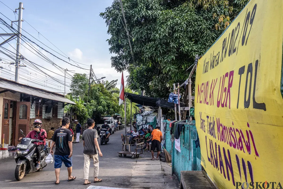 Warga beraktifitas melintasi spanduk penolakan uang ganti rugi tol Semanan Sunter di kawasan RW 09/12, Duri Pulo, Gambir, Jakarta Pusat, Selasa, 23 Desember 2025. (Sumber: Poskota/Dhiya Ahmad Fauzan)