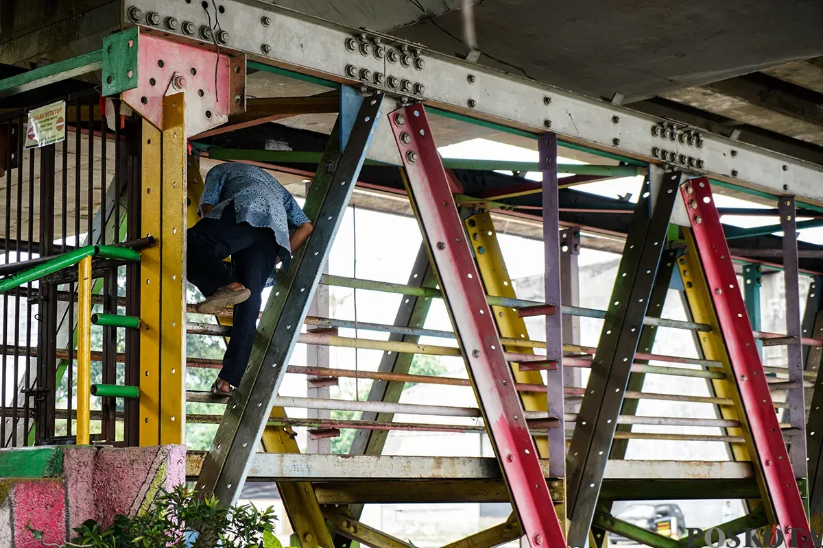 Warga berupaya menerobos pagar besi penutup dengan cara memanjat di Jembatan Penyebrangan Orang (JPO) Kolong Flyover Kalibata, Jakarta Selatan, Selasa, 4 Februari 2025. (Sumber: Poskota/Bilal Nugraha Ginanjar)