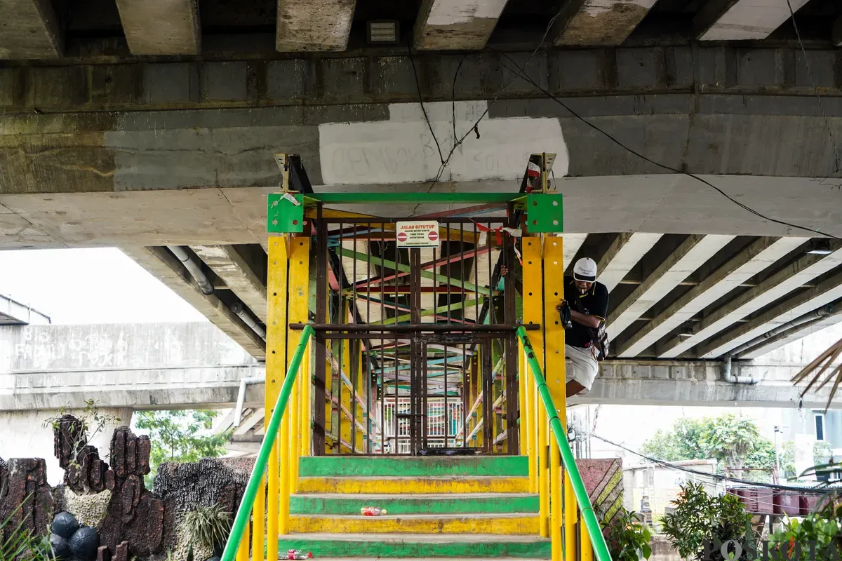 Warga berupaya menerobos pagar besi penutup dengan cara memanjat di Jembatan Penyebrangan Orang (JPO) Kolong Flyover Kalibata, Jakarta Selatan, Selasa, 4 Februari 2025. (Sumber: Poskota/Bilal Nugraha Ginanjar)