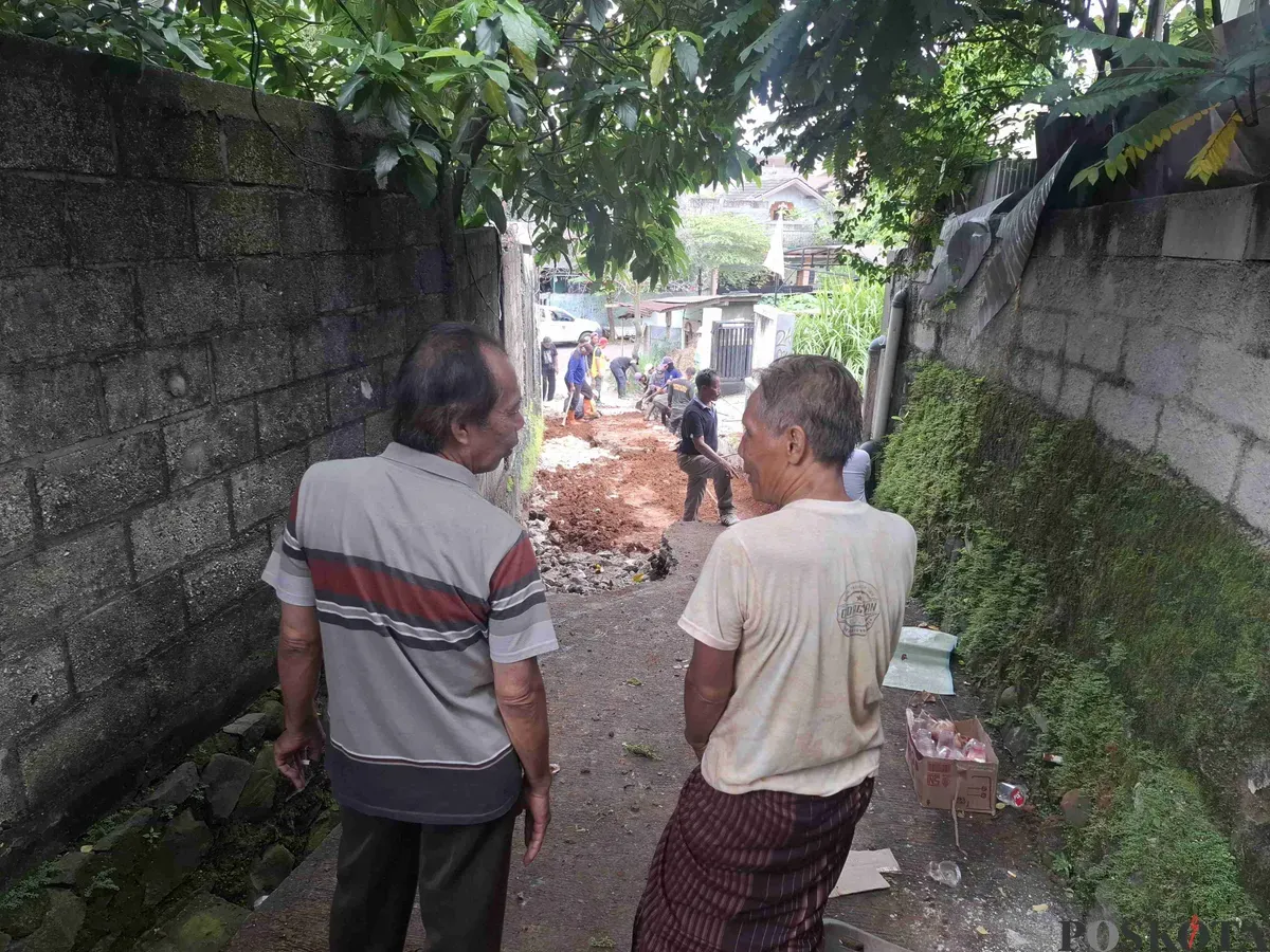 Heri (kanan) bersama warga sedang melihat jalan yang amblas di lingkungan mereka sedang diperbaiki oleh Dinas PUPR Kota Depok, Jumat siang, 14 Februari 2025. (Sumber: Poskota/Angga Pahlevi)