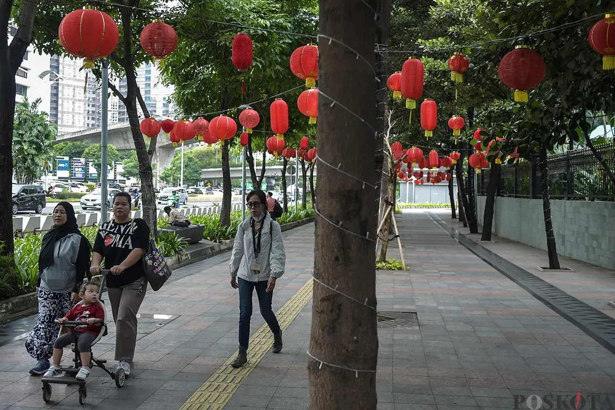 Pejalan kaki melintas di bawah ratusan lampion yang terpasang di antara pepohonan di trotoar Jalan Sudirman, Jakarta, Jumat, 17 Januari, 2025. (Sumber: Poskota/Bilal Nugraha Ginanjar)