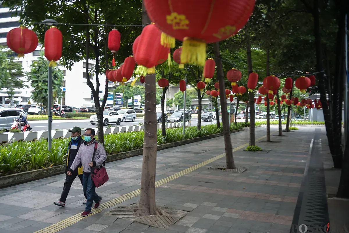 Pejalan kaki melintas di bawah ratusan lampion yang terpasang di antara pepohonan di trotoar Jalan Sudirman, Jakarta, Jumat, 17 Januari, 2025. (Sumber: Poskota/Bilal Nugraha Ginanjar)