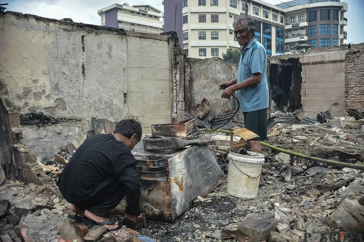 Sejumlah warga menyaksikan proses pendinginan terhadap puing-puing rumah yang terbakar yang dilakukan oleh petugas pemadam kebakaran usai terjadi musibah kebakaran di permukiman padat penduduk di Jalan Kemayoran Gempol, Kemayoran, Jakarta, Selasa, 21 Januari 2025. (Sumber: Poskota/ Bilal Nugraha Ginanjar)