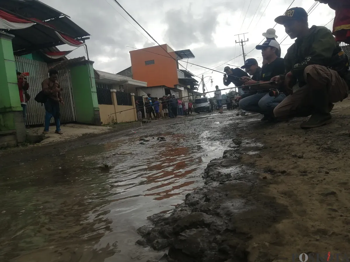 Warga Desa Wangunharja, Kecamatan Lembang, Kabupaten Bandung Barat memancing di tengah jalan yang tergenang air sebagai aksi protes akibat jalan rusak. (Sumber: Poskota/Gatot Poedji Utomo)