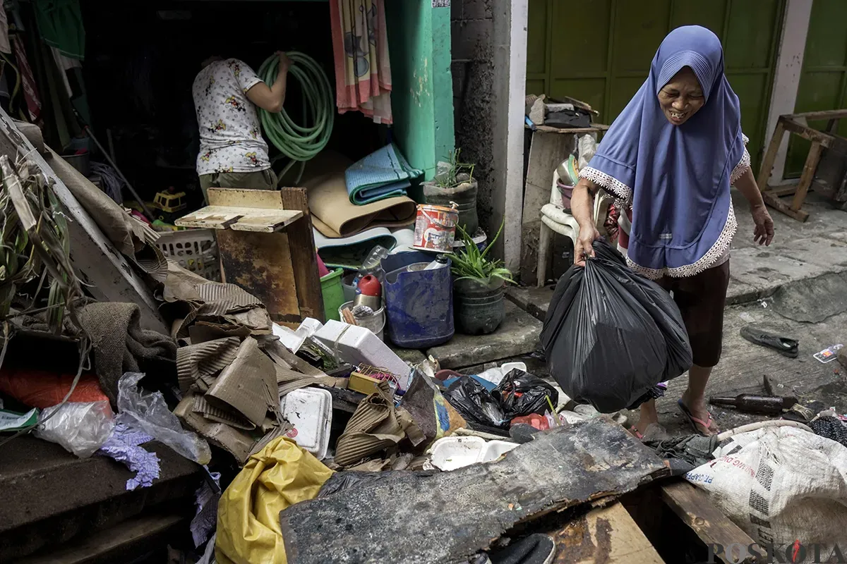 Petugas Penanganan Prasarana dan Sarana Umum (PPSU) Kelurahan Kapuk, mengangkut tumpukan sisa sampah yang terbawa arus air banjir di area gang permukiman pada penduduk di kawasan Jalan Kapuk Bongkaran, Cengkareng, Jakarta Barat, Kamis, 30 Januari 2025. (Sumber: Poskota/ Bilal Nugraha Ginanjar)