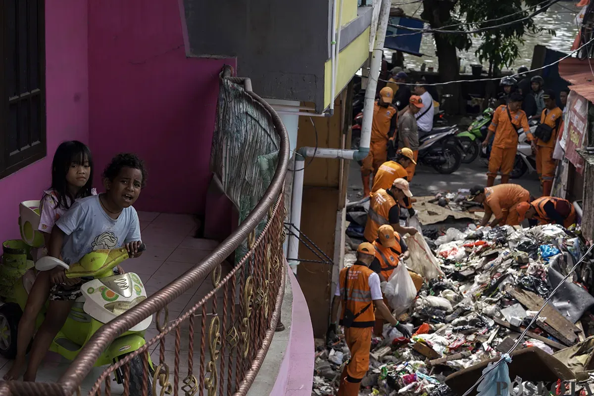 Petugas Penanganan Prasarana dan Sarana Umum (PPSU) Kelurahan Kapuk, mengangkut tumpukan sisa sampah yang terbawa arus air banjir di area gang permukiman pada penduduk di kawasan Jalan Kapuk Bongkaran, Cengkareng, Jakarta Barat, Kamis, 30 Januari 2025. (Sumber: Poskota/ Bilal Nugraha Ginanjar)