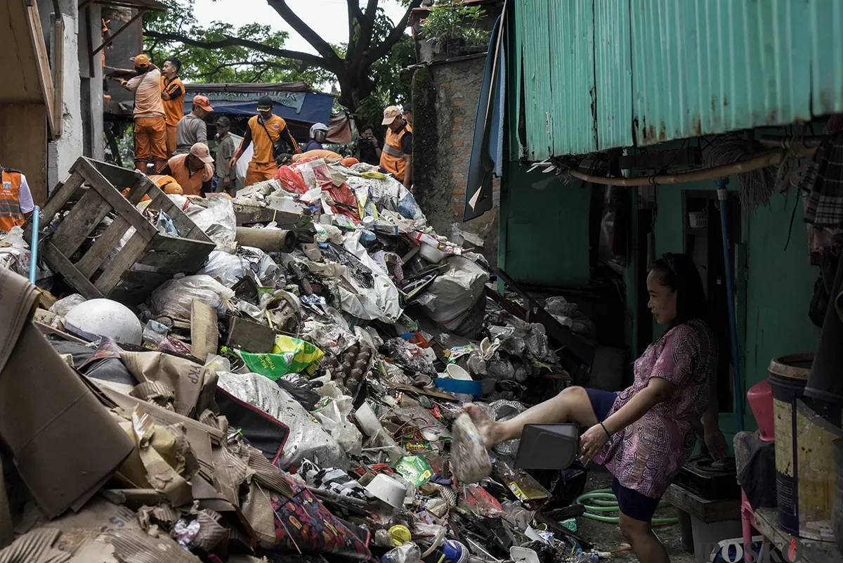 Petugas Penanganan Prasarana dan Sarana Umum (PPSU) Kelurahan Kapuk, mengangkut tumpukan sisa sampah yang terbawa arus air banjir di area gang permukiman pada penduduk di kawasan Jalan Kapuk Bongkaran, Cengkareng, Jakarta Barat, Kamis, 30 Januari 2025. (Sumber: Poskota/ Bilal Nugraha Ginanjar)