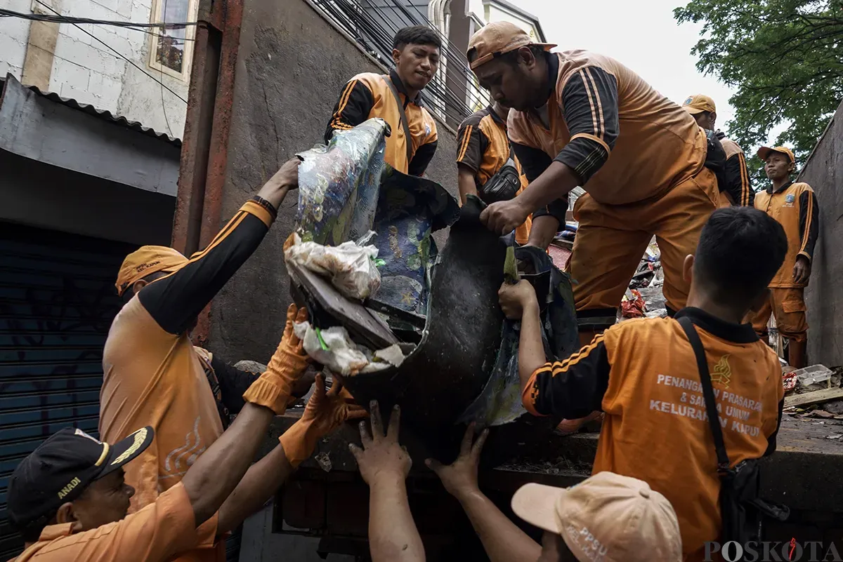 Petugas Penanganan Prasarana dan Sarana Umum (PPSU) Kelurahan Kapuk, mengangkut tumpukan sisa sampah yang terbawa arus air banjir di area gang permukiman pada penduduk di kawasan Jalan Kapuk Bongkaran, Cengkareng, Jakarta Barat, Kamis, 30 Januari 2025. (Sumber: Poskota/ Bilal Nugraha Ginanjar)