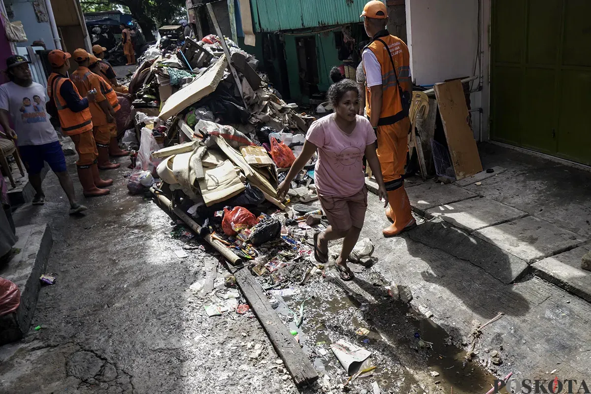 Petugas Penanganan Prasarana dan Sarana Umum (PPSU) Kelurahan Kapuk, mengangkut tumpukan sisa sampah yang terbawa arus air banjir di area gang permukiman pada penduduk di kawasan Jalan Kapuk Bongkaran, Cengkareng, Jakarta Barat, Kamis, 30 Januari 2025. (Sumber: Poskota/ Bilal Nugraha Ginanjar)