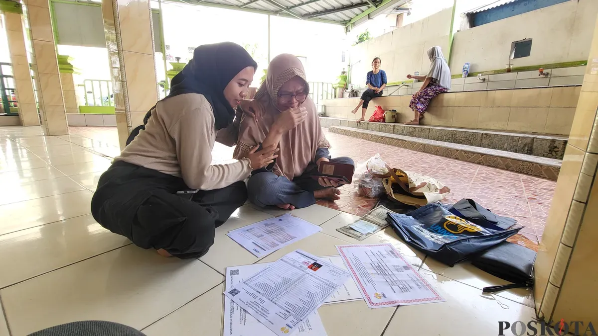 Diah (kanan) menangis sambil mengeringkan ijazah anaknya yang terendam banjir di pengungsian Masjid An Nur, Cengkareng, Jakarta Barat, Jumat, 31 Januari 2025. (Sumber: Poskota/Pandi Ramedhan)