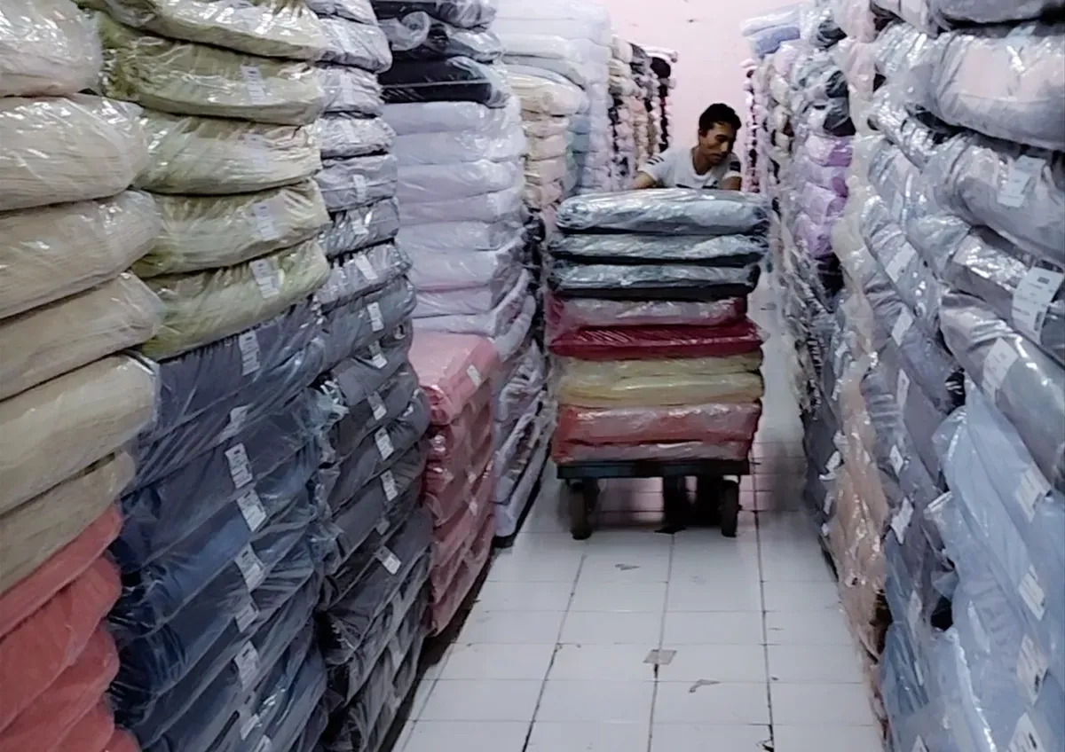 Pekerja Focus Textile mendorong tumpukan kain yang dikemas rapi di salah satu gudang. Industri tekstil tetap beroperasi di tengah tekanan ekonomi dan persaingan impor. (Sumber: Istimewa)