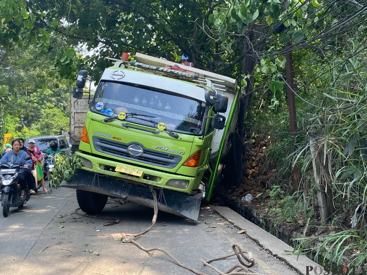Truk Hino berwarna hijau-putih terperosok ke parit setelah gagal menanjak di Tanjakan Parakan, Pamulang, Tangerang Selatan, pada Jumat, 4 Juli 2025. (Sumber: Poskota/Primayanti Juli Kumala Manalu)