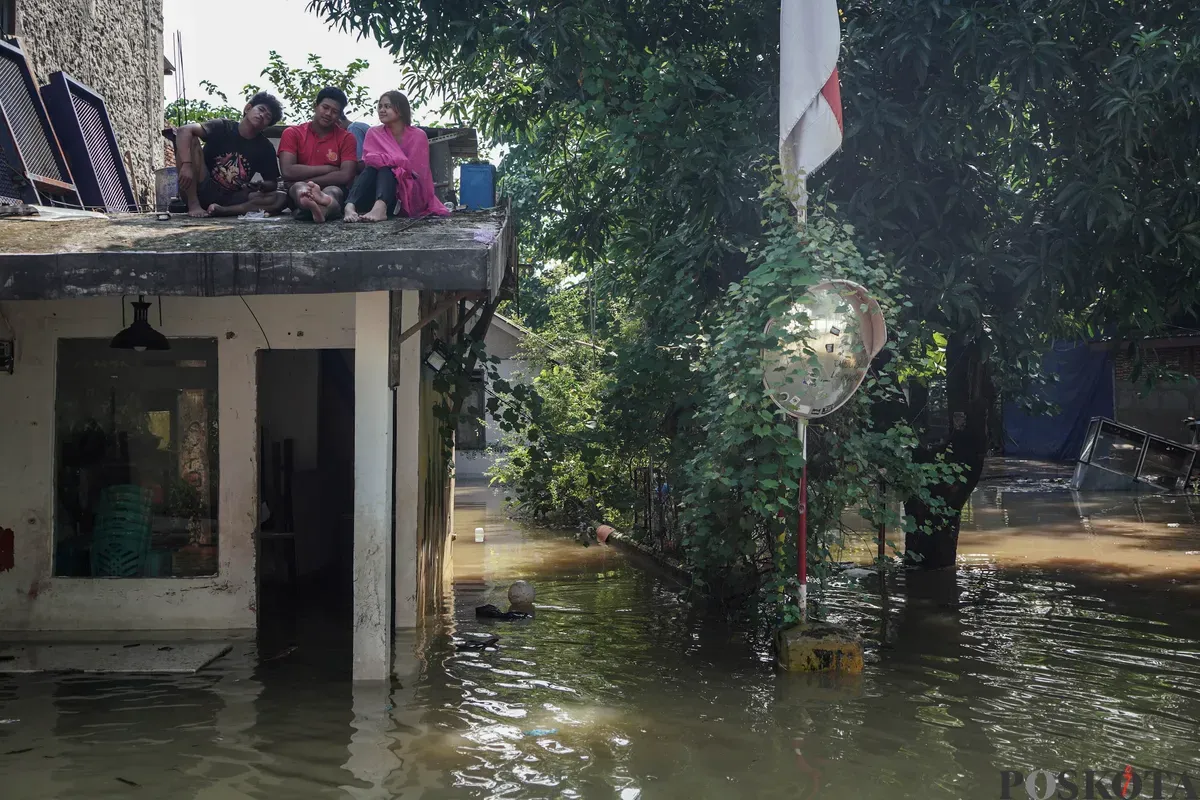 Warga duduk diatas rumah yang tergenang banjir di Jalan Pirus, Bidara Cina, Jatinegara, Jakarta Timur, Minggu, 8 Juli 2025. (Sumber: Poskota/Bilal Nugraha Ginanjar)