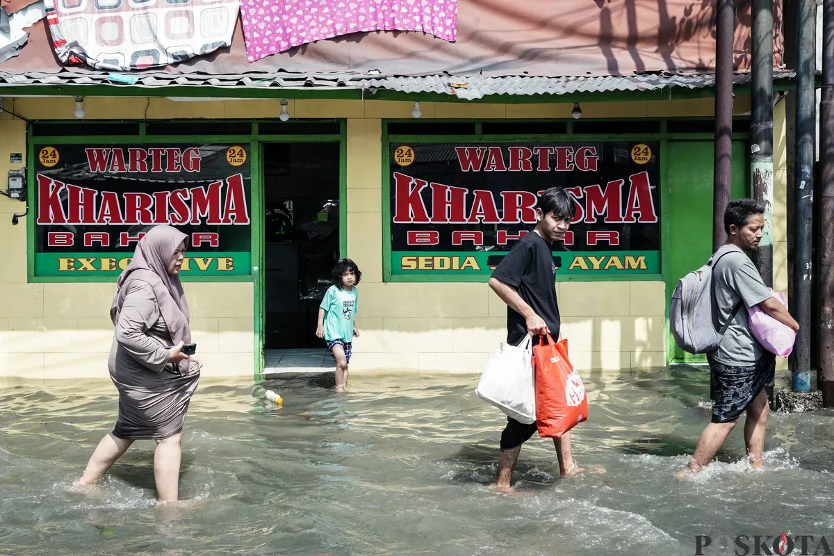 Warga berjalan melintasi banjir di Kampung Makasar, Jakarta Timur, Senin, 7 Juli 2025. (Sumber: Poskota/Bilal Nugraha Ginanjar)
