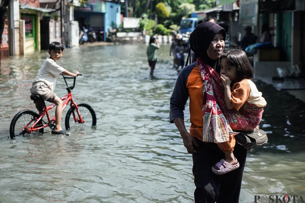 Warga berjalan melintasi banjir di Kampung Makasar, Jakarta Timur, Senin, 7 Juli 2025. (Sumber: Poskota/Bilal Nugraha Ginanjar)