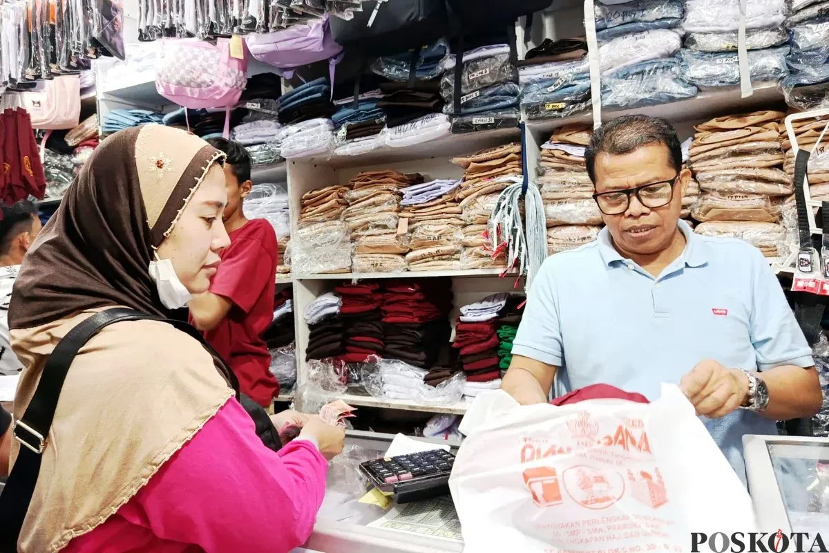 Anies, 54 Tahun, pemilik toko seragam sekolah sedang melayani pelanggan di Pasar Baru Bekasi, Minggu, 13 Juli 2025. (Sumber: Poskota/Nurpini Aulia Rapika)