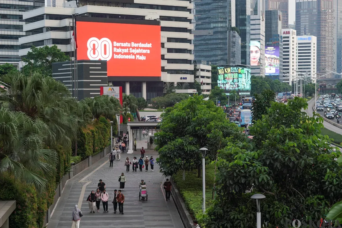 Sejumlah warga melintas di dekat Videotron yang menampilkan logo HUT RI ke-80 di kawasan Jalan Sudirman, Jakarta, Kamis, 24 Juli 2025. (Sumber: Poskota/Bilal Nugraha Ginanjar)
