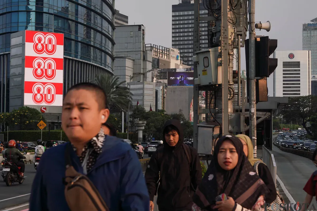 Sejumlah warga melintas di dekat Videotron yang menampilkan logo HUT RI ke-80 di kawasan Jalan Sudirman, Jakarta, Kamis, 24 Juli 2025. (Sumber: Poskota/Bilal Nugraha Ginanjar)