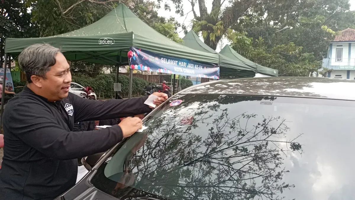 Petugas DLH Kota Cimahi memasang stiker tanda lolos uji emisi pada kendaraan. (Sumber: POSKOTA | Foto: Gatot Poedji Utomo)