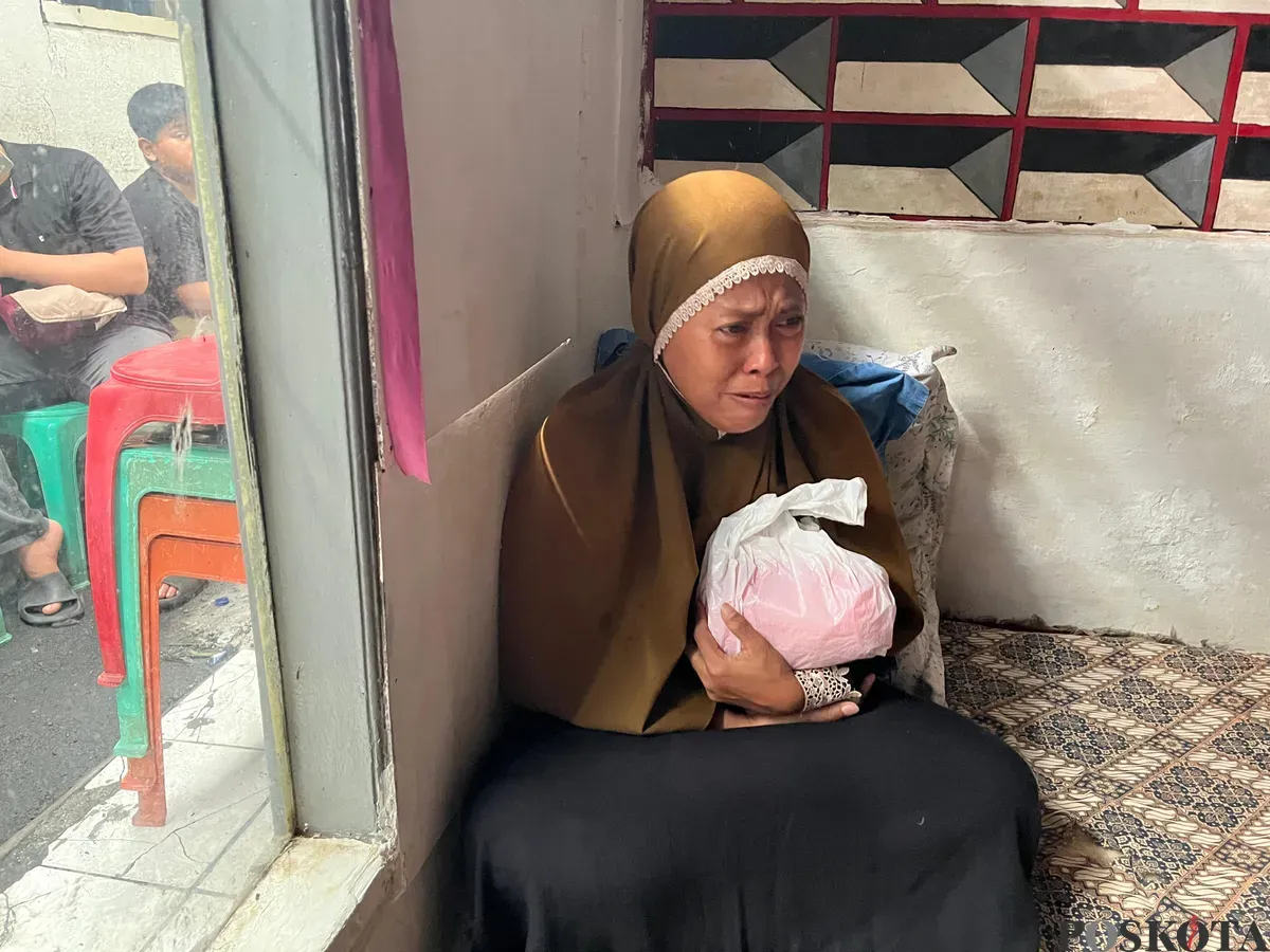 Nurjanah, 49 tahun, orangtua korban kebakaran rumah tinggal di Tebet, Jaksel, sedang menggendog buntelan plastik berisikan bagian tubuh anaknya yang terbakar, Kamis, 19 Juni 2025. (Sumber: Poskota/Pandi Ramedhan)