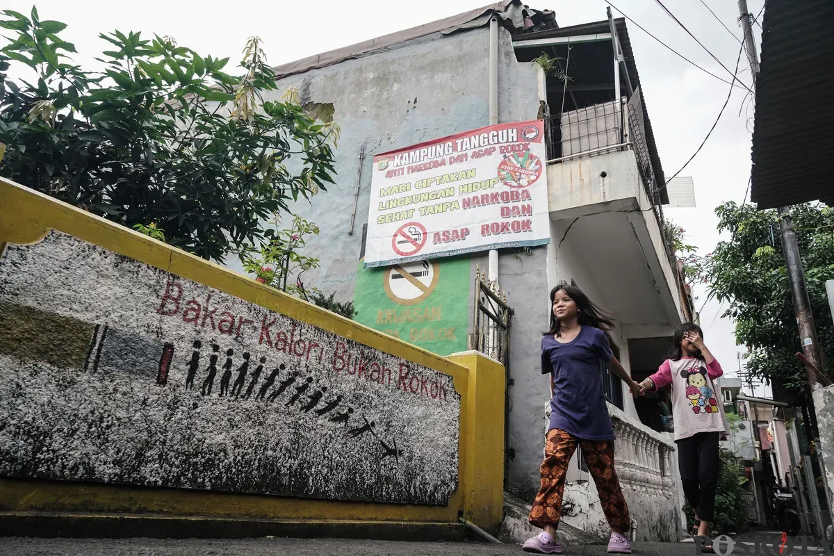 Warga berjalan melewati mural anti rokok di permukiman padat penduduk Matraman, Jakarta, 24 Juni 2025. (Sumber: Poskota/Bilal Nugraha Ginanjar)