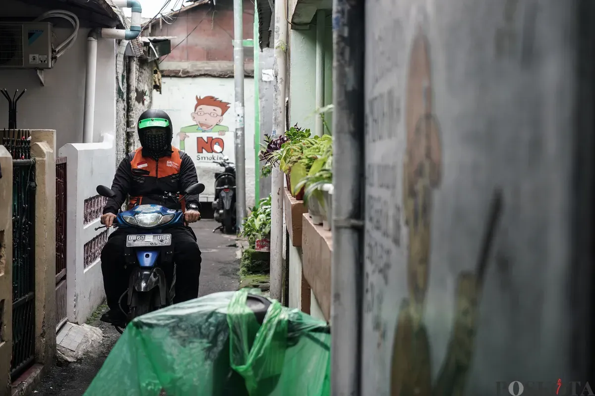 Warga berjalan melewati mural anti rokok di permukiman padat penduduk Matraman, Jakarta, 24 Juni 2025. (Sumber: Poskota/Bilal Nugraha Ginanjar)