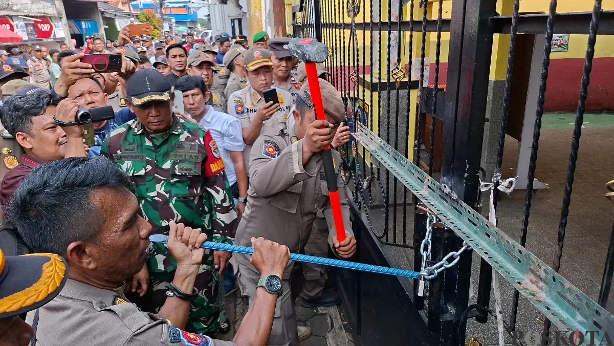 Petugas Satpol PP Kota Depok menggunakan linggis untuk membongkar paksa rantai yang mengunci gerbang SDN Utan Jaya, Cipayung, Kota Depok, Kamis, 8 Mei 2025. (Sumber: Poskota/Angga Pahlevi)