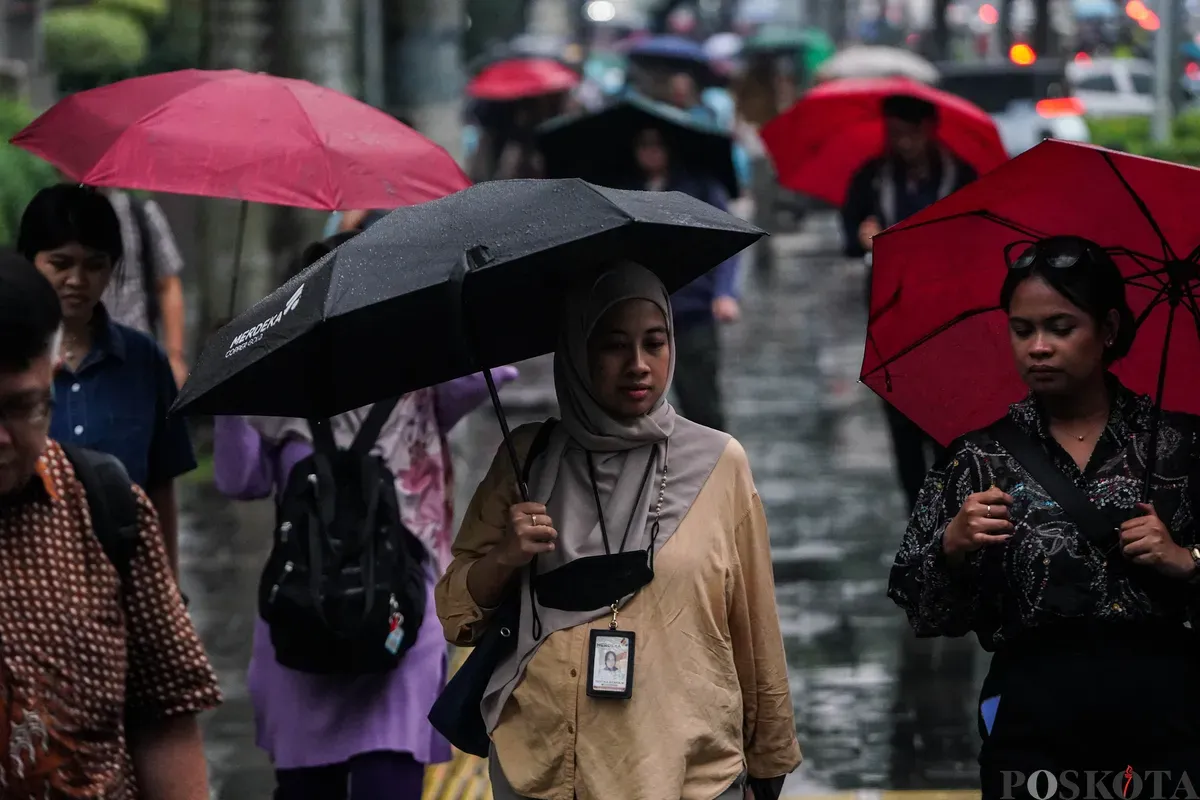 Warga berjalan dengan menggunakan payung di trotoar Jalan Sudirman, Jakarta, Rabu, 21 Mei 2025. (Sumber: Poskota/Bilal Nugraha Ginanjar)