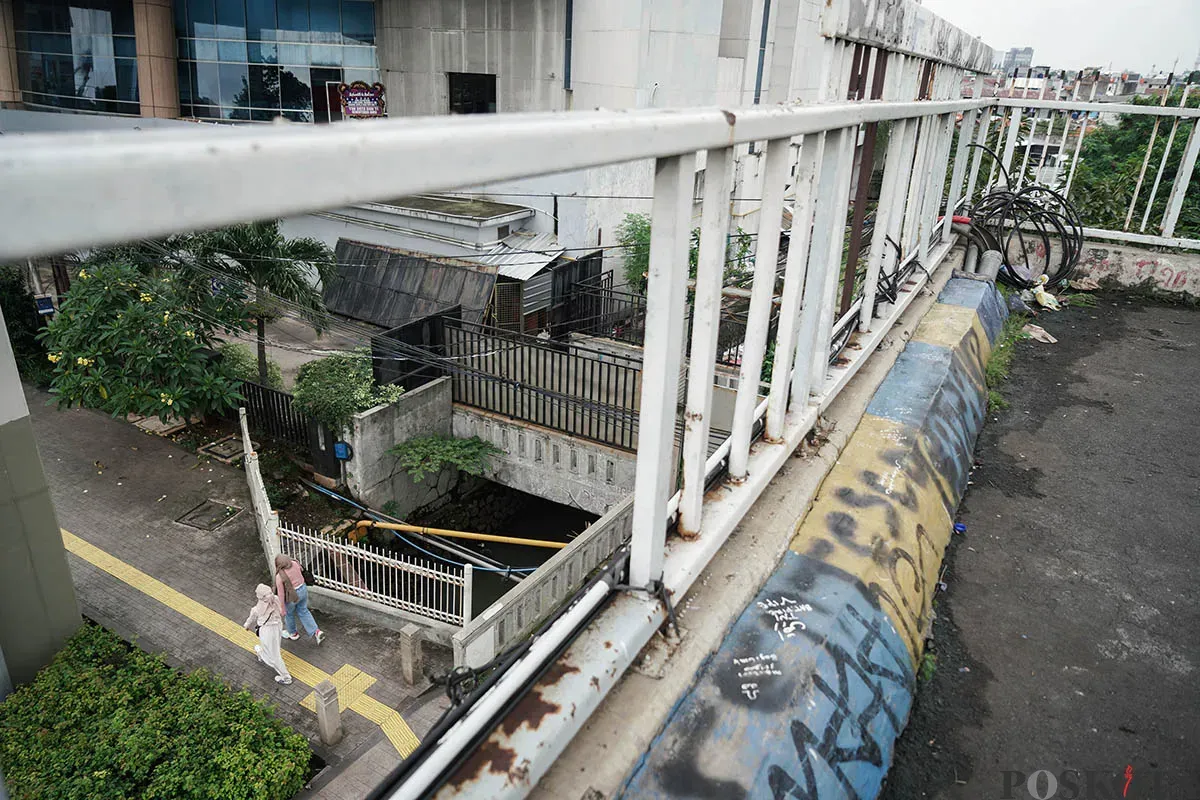 Warga berjalan diatas Jembatan Penyebrangan Orang (JPO) di depan Gedung Smesco, Jalan Gatot Subroto, Jakarta Selatan, tak terawat, Minggu, 25 Mei 2025. (Sumber: Poskota/Bilal Nugraha Ginanjar)
