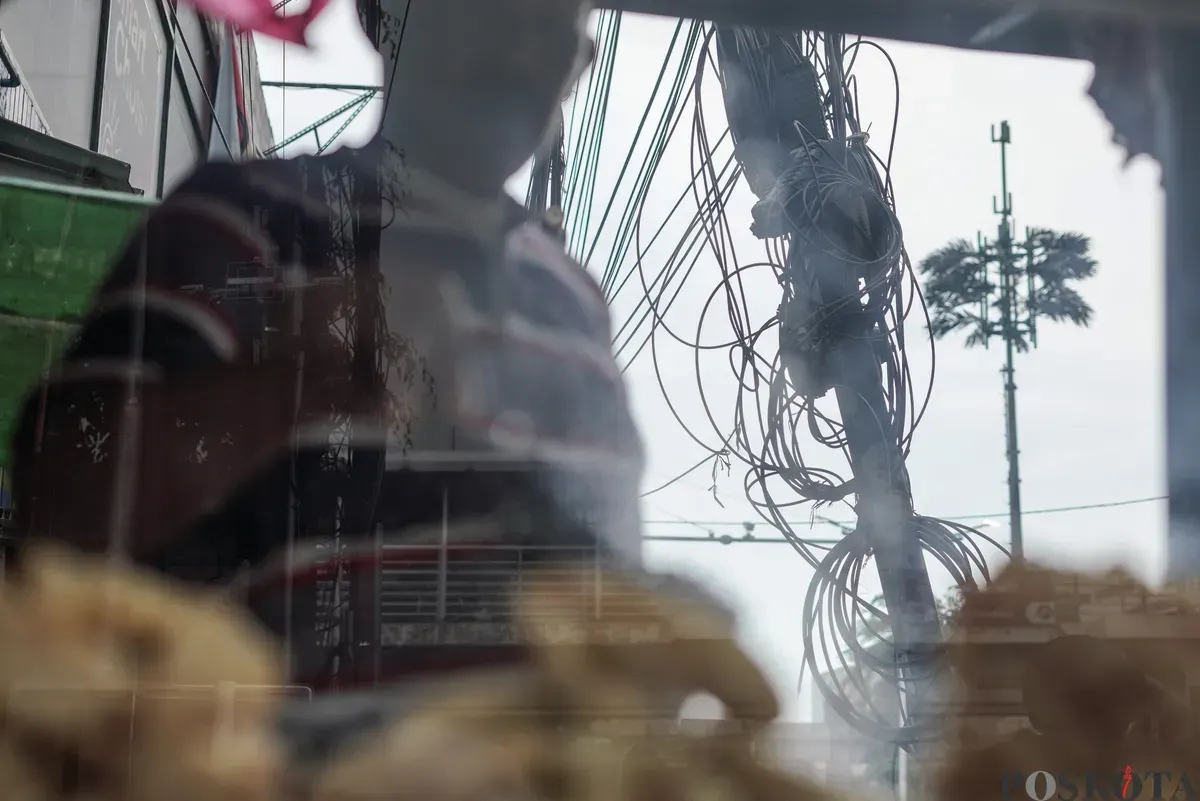Jaringan kabel utilitas yang menjuntai semrawut di jalur pedestrian kawasan Otista Raya, Jakarta Timur, Minggu, 1 November 2025. (Sumber: Poskota/Bilal Nugraha Ginanjar)