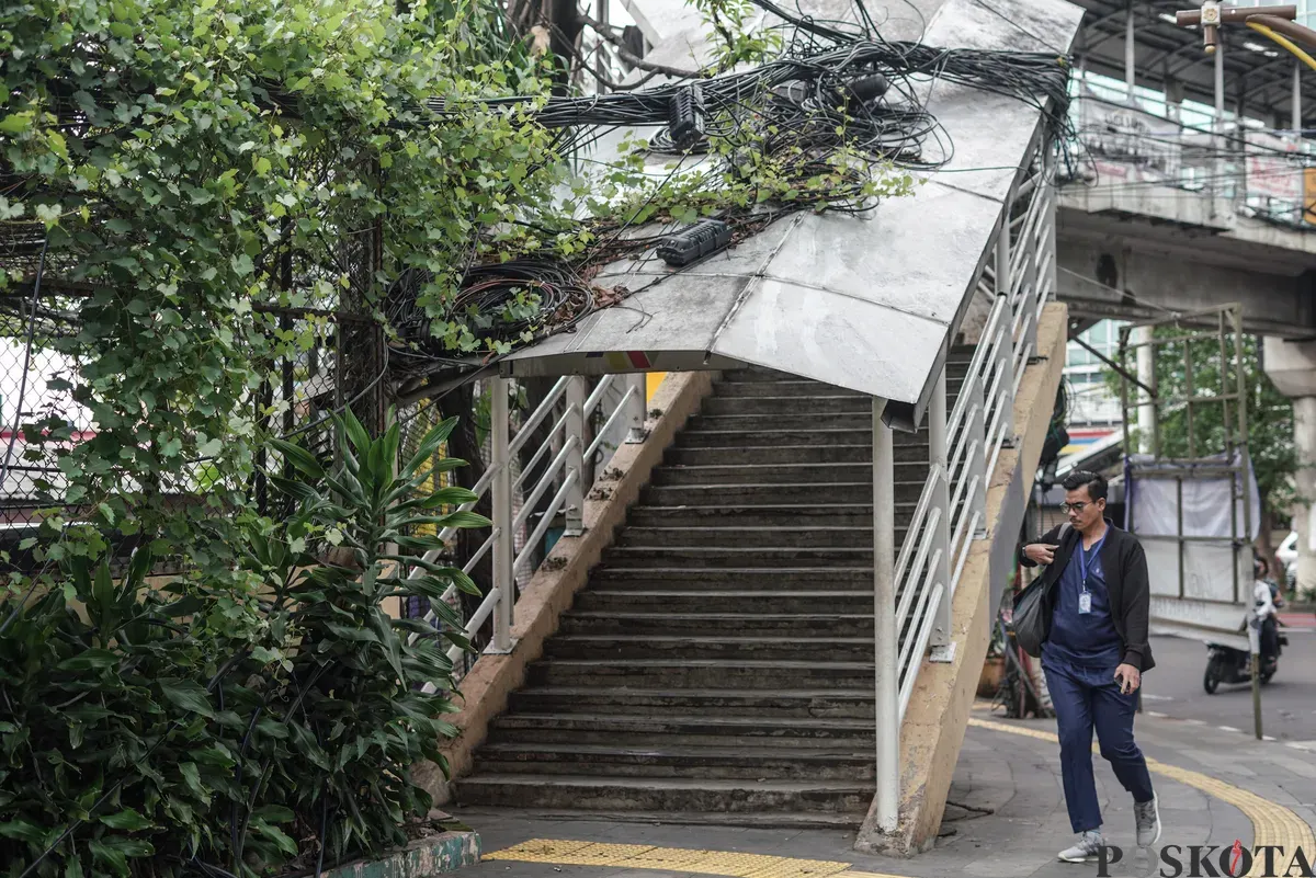Jaringan kabel utilitas yang menjuntai semrawut di jalur pedestrian kawasan Otista Raya, Jakarta Timur, Minggu, 1 November 2025. (Sumber: Poskota/Bilal Nugraha Ginanjar)