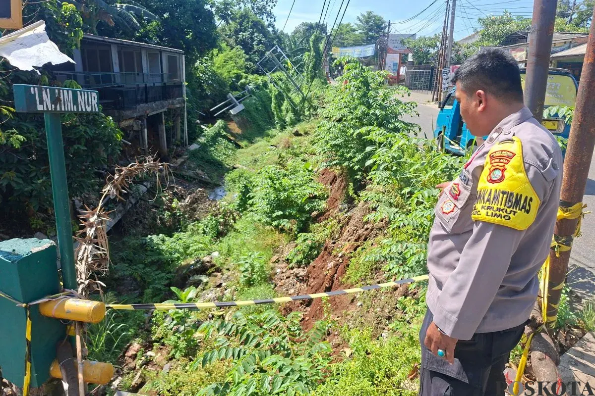 Petugas kepolisian menunjukan tebing longsor di Jalan Raya Krukut RT 04/RW 01, Kelurahan Krukut. Kecamatan Limo, Kota Depok, Selasa, 4 November 2025. (Sumber: Poskota/Angga Pahlevi)