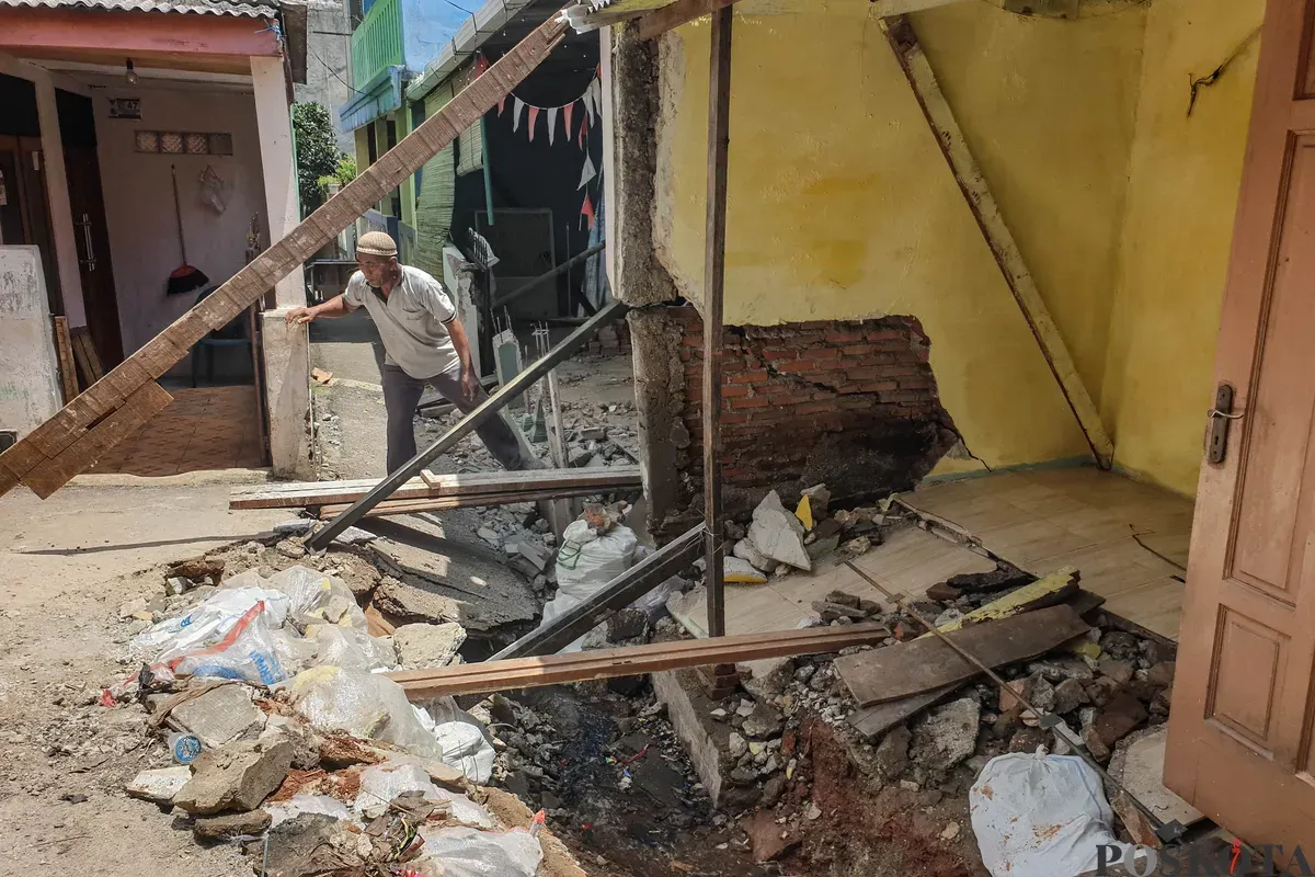 Warga membersihkan puing - puing rumahnya yang hancur akibat pergerakan tanah di Gang Sumur Jambu, Makasar, Jakarta Timur. (Sumber: Poskota/Bilal Nugraha Ginanjar)