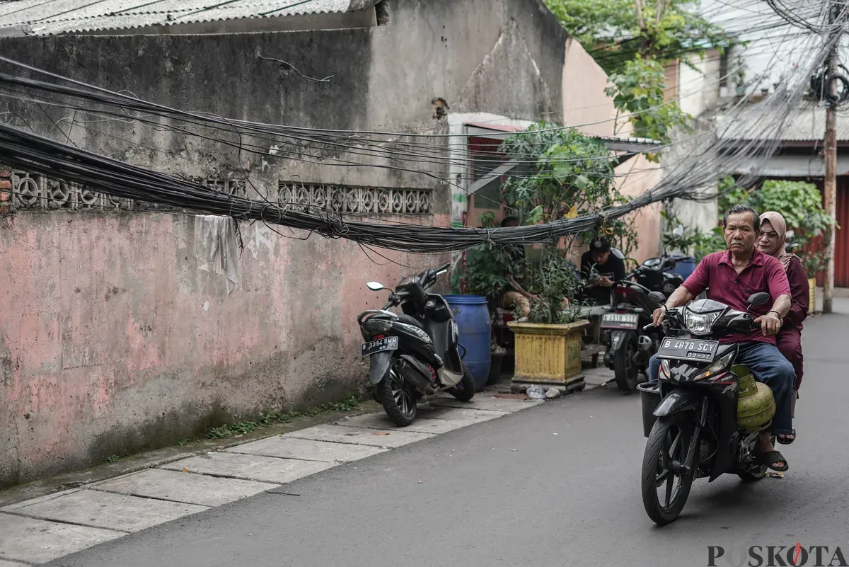 Warga melintas di dekat jaringan utilitas yang menjuntai di Jalan Anggrek II, Karet Kuningan, Setiabudi, Jakarta, Selasa, 11 November 2025. (Sumber: Poskota/Bilal Nugraha Ginanjar)