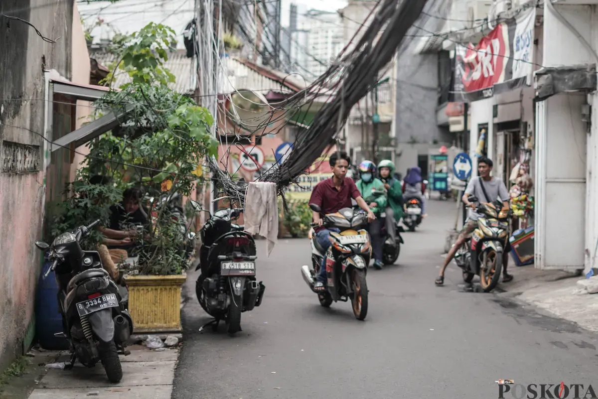 Warga melintas di dekat jaringan utilitas yang menjuntai di Jalan Anggrek II, Karet Kuningan, Setiabudi, Jakarta, Selasa, 11 November 2025. (Sumber: Poskota/Bilal Nugraha Ginanjar)