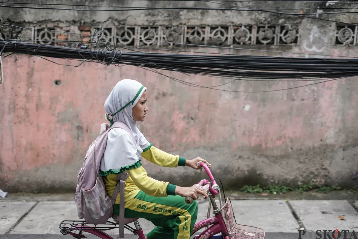 Warga melintas di dekat jaringan utilitas yang menjuntai di Jalan Anggrek II, Karet Kuningan, Setiabudi, Jakarta, Selasa, 11 November 2025. (Sumber: Poskota/Bilal Nugraha Ginanjar)