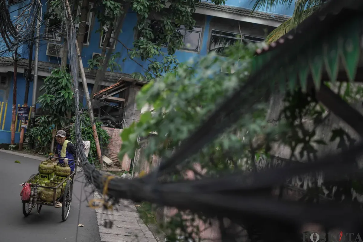 Warga melintas di dekat jaringan utilitas yang menjuntai di Jalan Anggrek II, Karet Kuningan, Setiabudi, Jakarta, Selasa, 11 November 2025. (Sumber: Poskota/Bilal Nugraha Ginanjar)