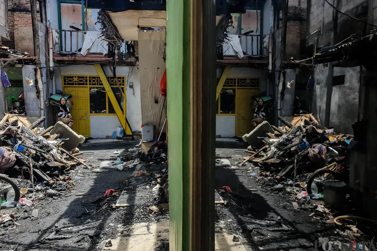 Warga berjalan di sekitar lokasi kebakaran akibat putusnya ground steel wire jaringan saluran udara tegangan tinggi di RW 004 Jatipulo, Jakarta Barat, Senin, 17 November 2025. (Sumber: Poskotra/Bilal Nugraha Ginanjar)