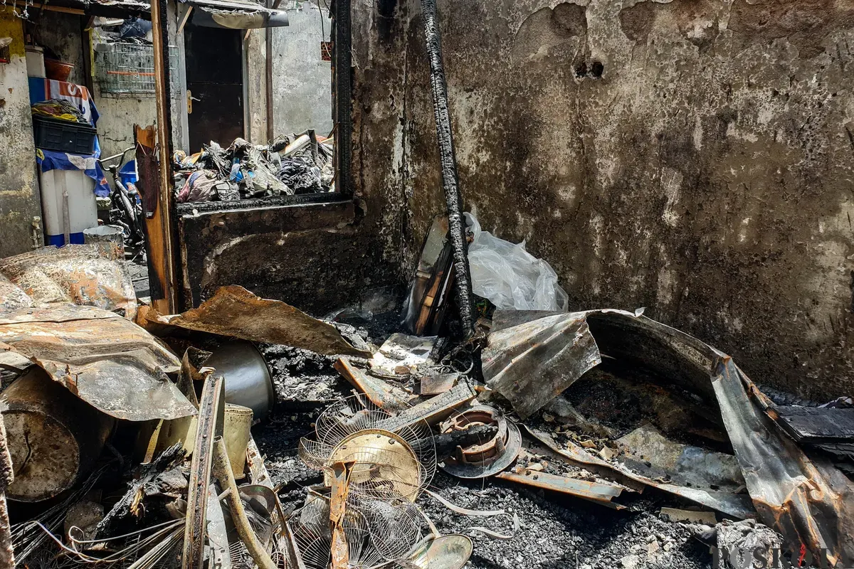 Warga berjalan di sekitar lokasi kebakaran akibat putusnya ground steel wire jaringan saluran udara tegangan tinggi di RW 004 Jatipulo, Jakarta Barat, Senin, 17 November 2025. (Sumber: Poskota/Bilal Nugraha Ginanjar)