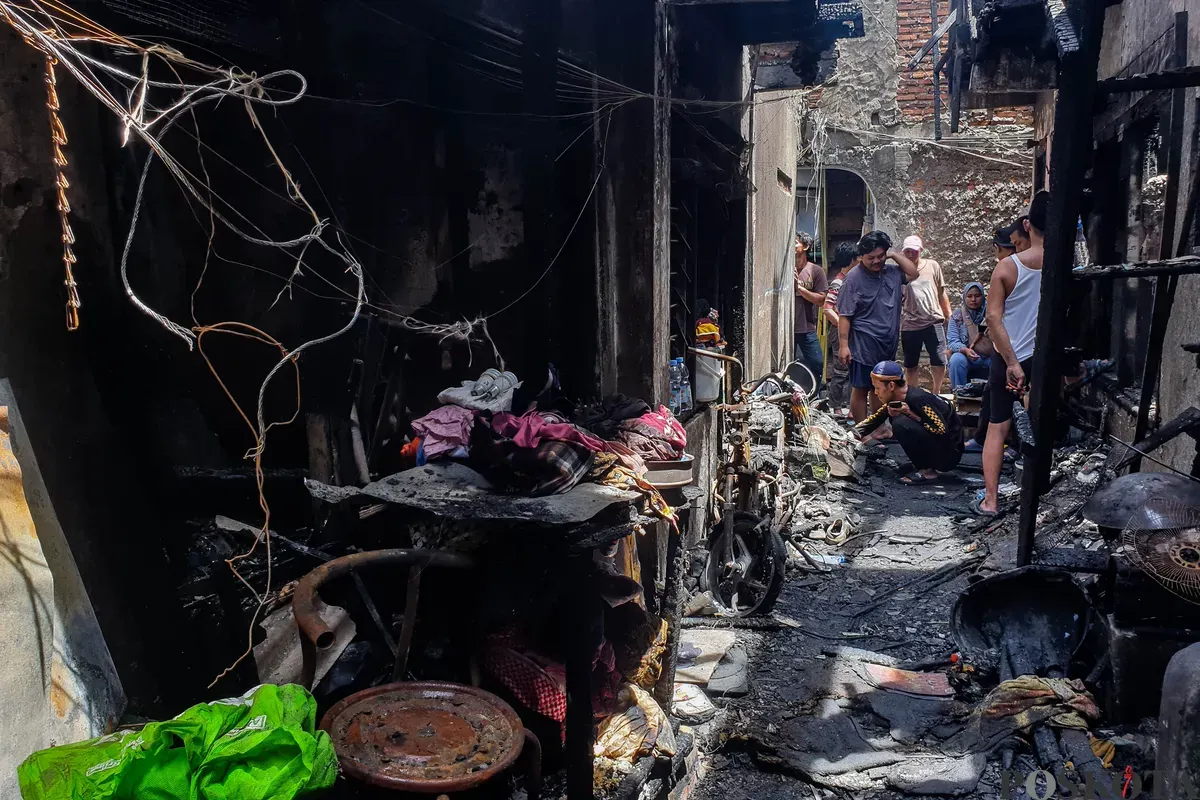 Warga berjalan di sekitar lokasi kebakaran akibat putusnya ground steel wire jaringan saluran udara tegangan tinggi di RW 004 Jatipulo, Jakarta Barat, Senin, 17 November 2025. (Sumber: Poskota/Bilal Nugraha Ginanjar)