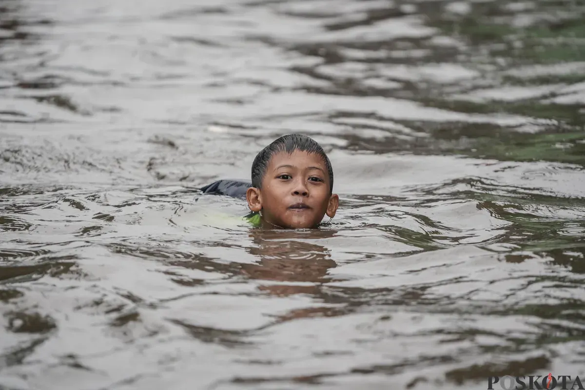 Seorang anak berenang pada genangan banjir di Kompleks Polri Pondok Karya, Mampang Prapatan, Jakarta, Selasa, 18 November 2025. (Sumber: Poskota/Bilal Nugraha Ginanjar)
