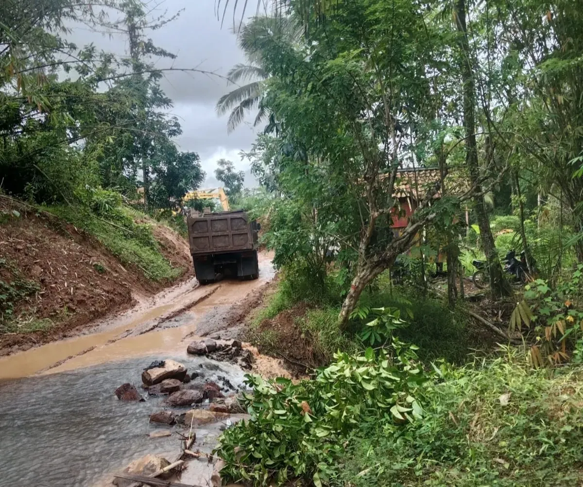 Sebuah truk melintas di jalan berlumpur dekat aliran air di Desa Cibitung, Munjul, Pandeglang. Warga menyebut material dari aktivitas tambang di area perbukitan kerap terbawa hujan dan menimbun lahan pertanian di sekitarnya. (Sumber: Istimewa)