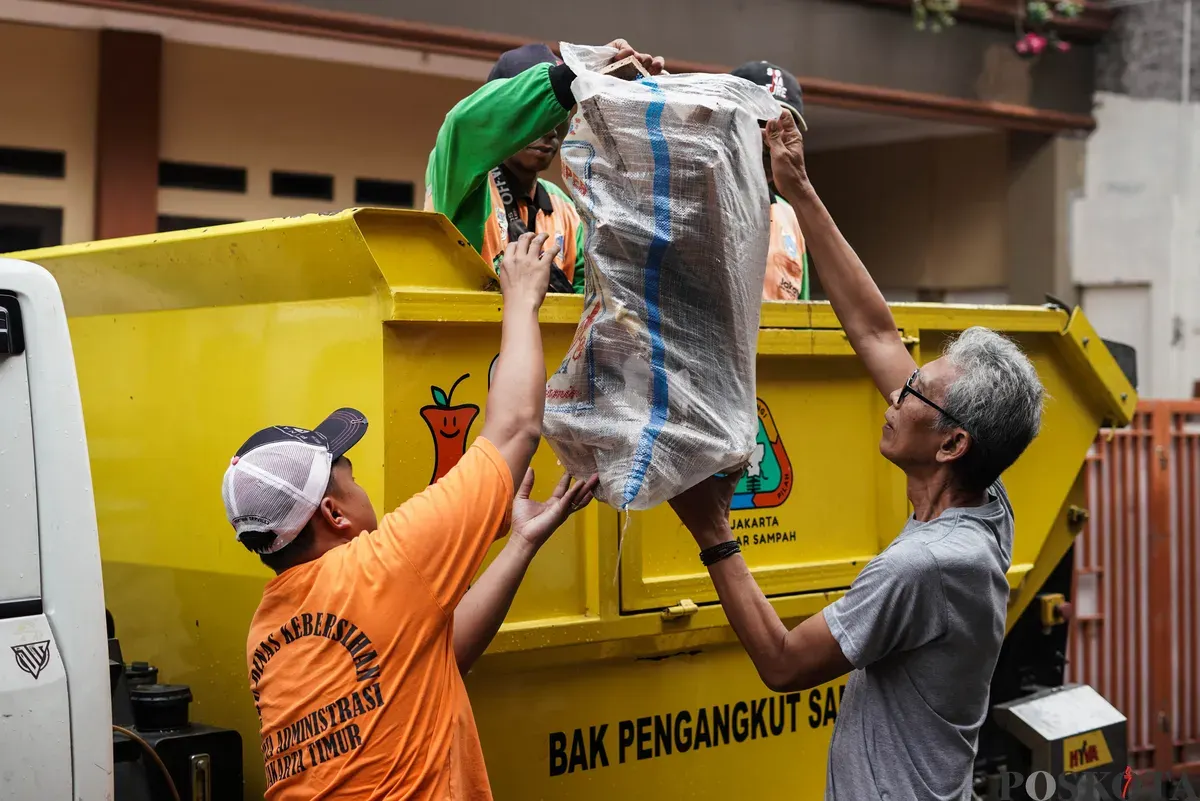 Petugas Dinas Lingkungan Hidup Kota Jakarta Timur dibantu warga mengangkut kayu lemari bekas milik warga menggunakan mobil truk di kawasan Cijantung, Pasar Rebo, Jakarta, Selasa, 21 Oktober 2025. (Sumber: Poskota/Bilal Nugraha Ginanjar)