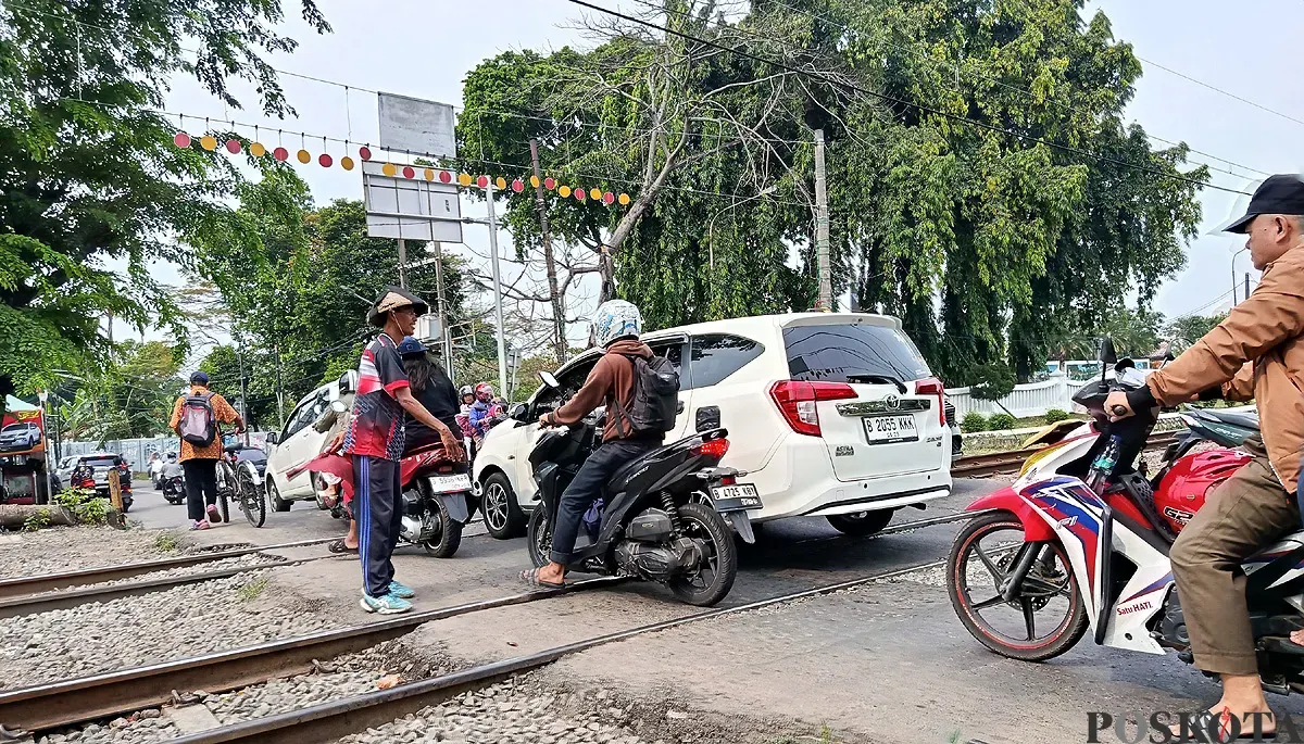Suasana pelintasan kereta Bulak Kapal, Bekasi Timur, tanpa palang pintu di kedua sisinya. Petugas bersama warga mengatur lalu lintas yang padat, Minggu 14 September 2025. (Sumber: POSKOTA | Foto: Nurpini Aulia Rapika)
